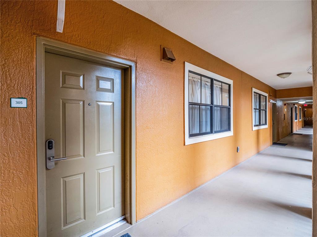 An exterior apartment hallway features orange stucco walls, a brown door numbered 305, and windows — 12539 FLORIDAYS RESORT DRIVE UNIT 305-D, ORLANDO, FL