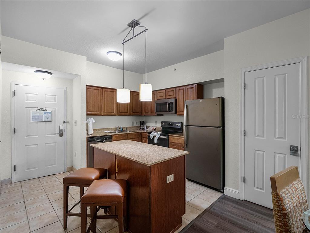 A kitchen features wood cabinets, stainless steel appliances, a granite-topped island, and two bar stools — 12539 FLORIDAYS RESORT DRIVE UNIT 305-D, ORLANDO, FL