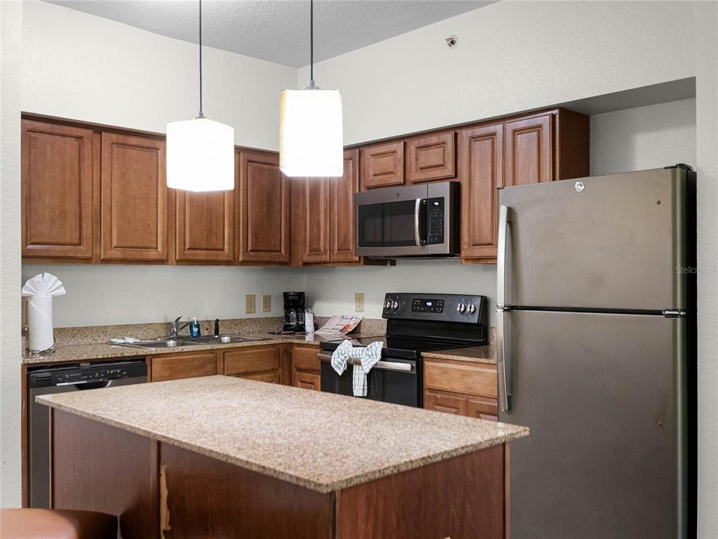 A kitchen features wood cabinets, granite countertops, stainless steel appliances, and a central island — 12539 FLORIDAYS RESORT DRIVE UNIT 305-D, ORLANDO, FL