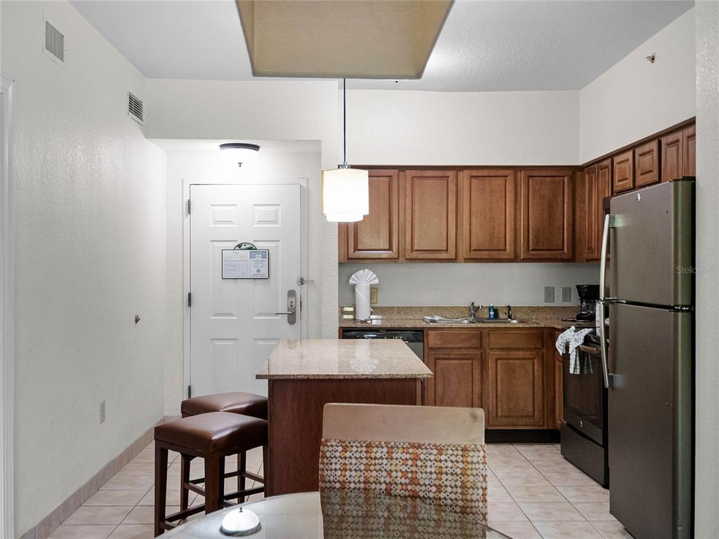 A kitchen features wood cabinets, granite countertops, a center island, and a stainless steel refrigerator — 12539 FLORIDAYS RESORT DRIVE UNIT 305-D, ORLANDO, FL