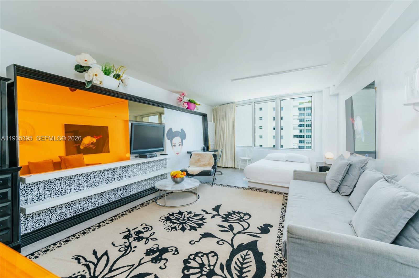 A studio apartment features a gray sofa, a bed, and a vibrant orange media wall — 1100 West Ave # 1004, Miami Beach FL 33139, MIAMI BEACH, FL