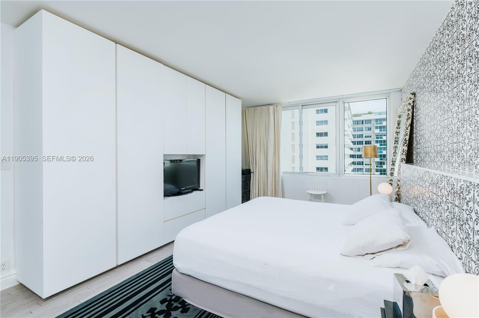 A bedroom features a large white wardrobe, a bed with white linens, and patterned wallpaper — 1100 West Ave # 1004, Miami Beach FL 33139, MIAMI BEACH, FL