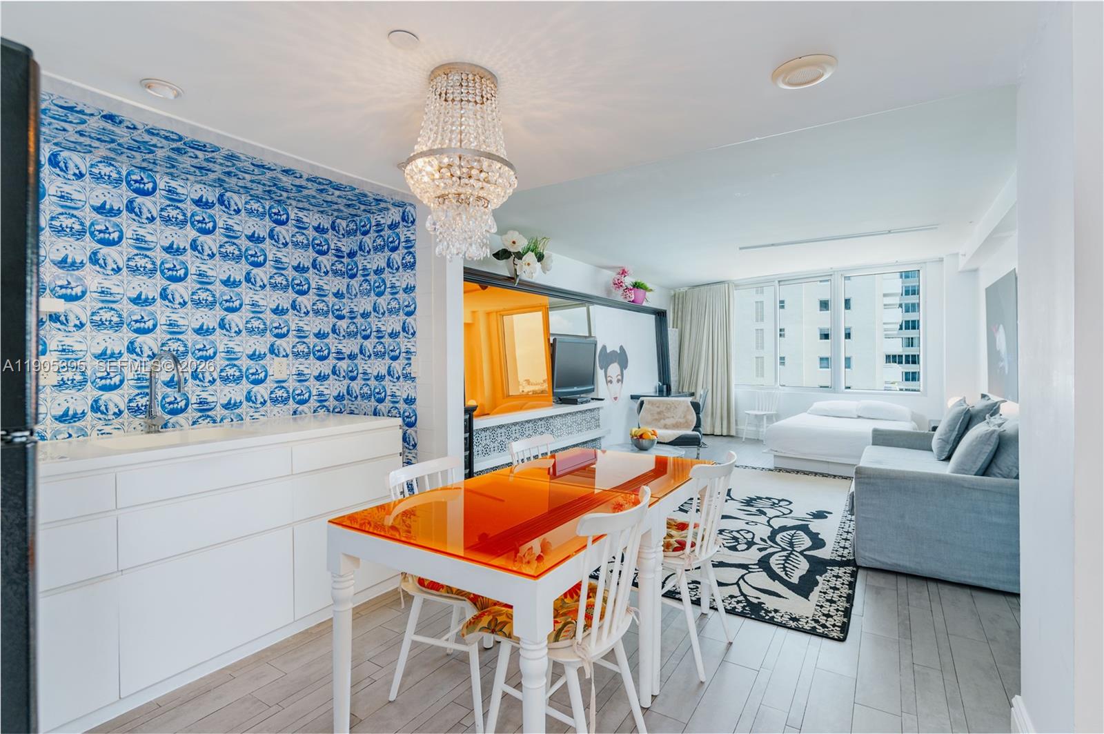 A studio apartment features a blue-tiled kitchen wall, an orange dining table, and a bed — 1100 West Ave # 1004, Miami Beach FL 33139, MIAMI BEACH, FL