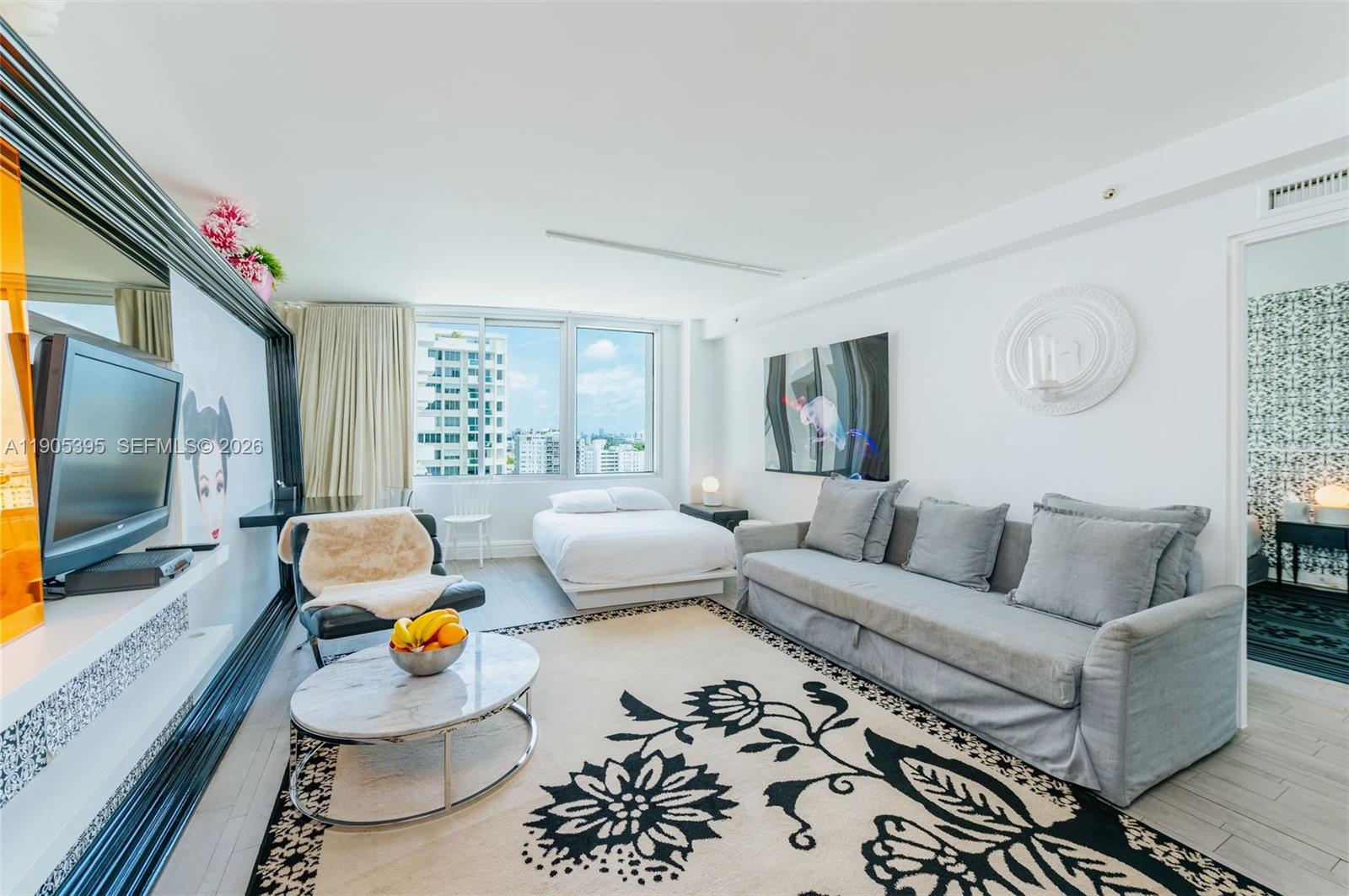 A studio apartment features a bed, a gray sofa, a patterned rug, and city views — 1100 West Ave # 1004, Miami Beach FL 33139, MIAMI BEACH, FL