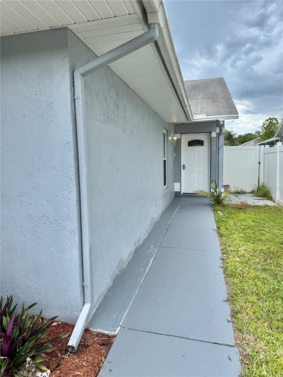 A gray exterior wall features a downspout, a white door, and a painted concrete walkway — 4811 PLINY COURT, KISSIMMEE, FL