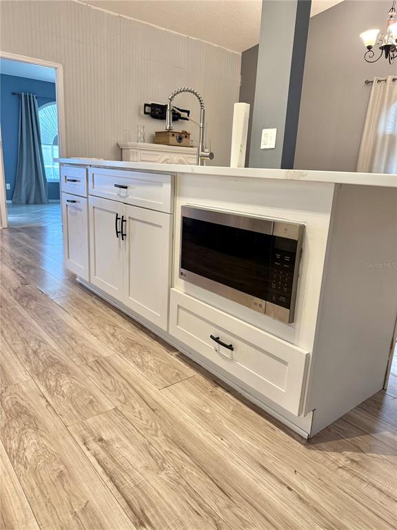 A kitchen island with white cabinets, a built-in microwave, and wood-look flooring — 4811 PLINY COURT, KISSIMMEE, FL