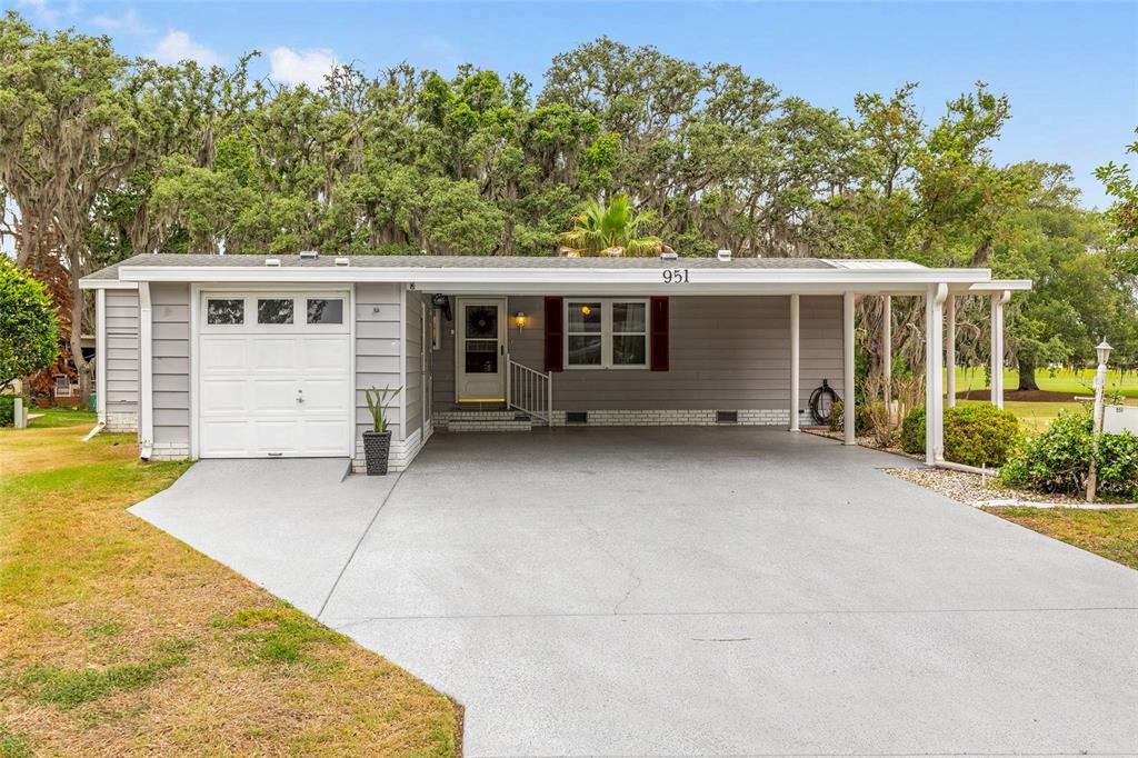 A single-story house with gray siding, a white garage door, and a covered carport — 951 OLEANDER STREET, LADY LAKE, FL