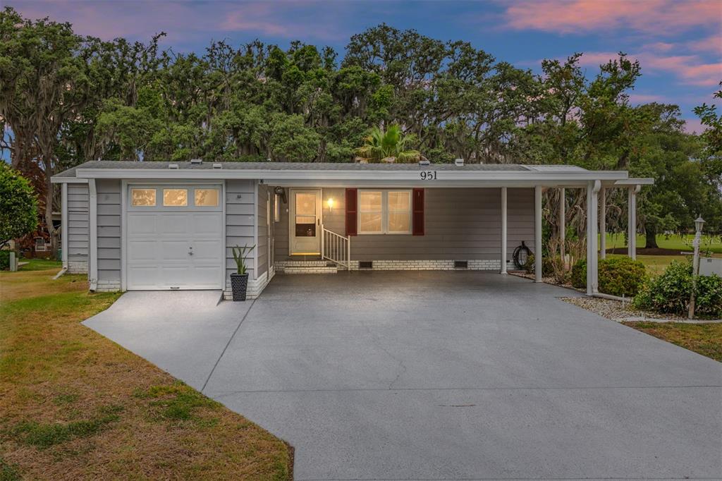 A single-story house with gray siding, a white garage door, and a covered carport — 951 OLEANDER STREET, LADY LAKE, FL