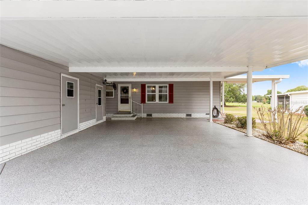 A covered carport with a gray speckled floor leads to the entrance of a house — 951 OLEANDER STREET, LADY LAKE, FL