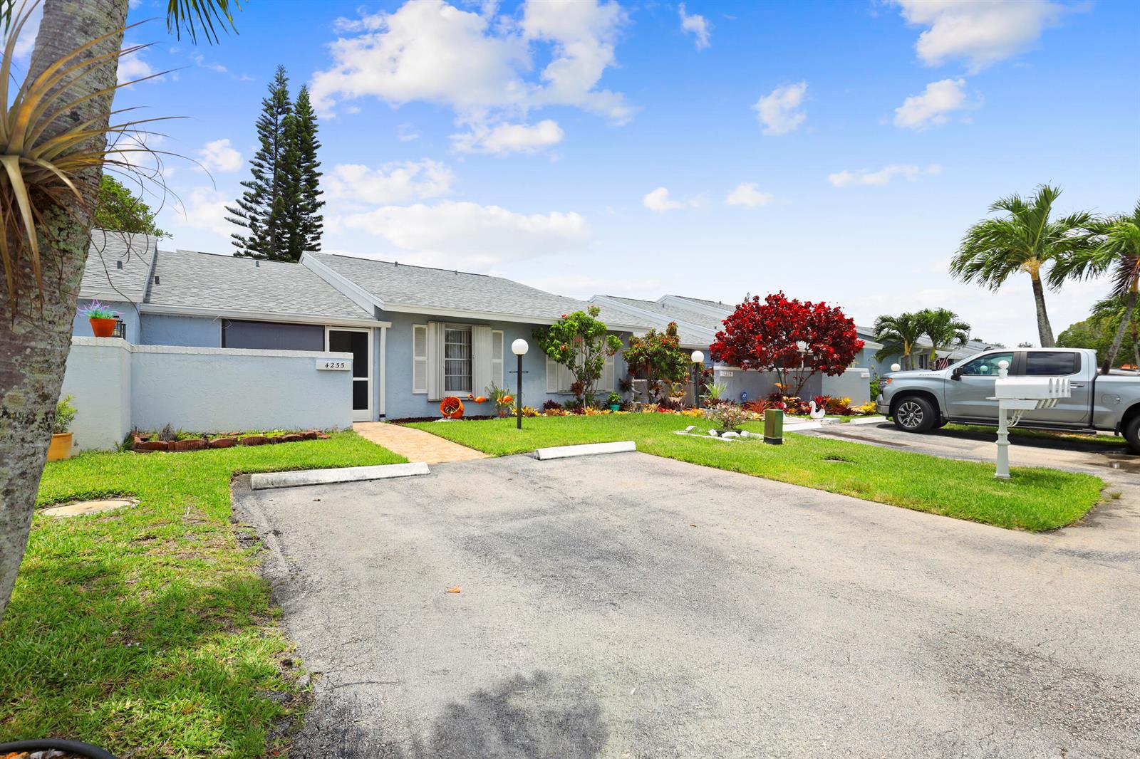 A light blue single-story house features a paved driveway, a front lawn, and landscaping — 4235 Lucerne Villas Lane, FL 33467, FL