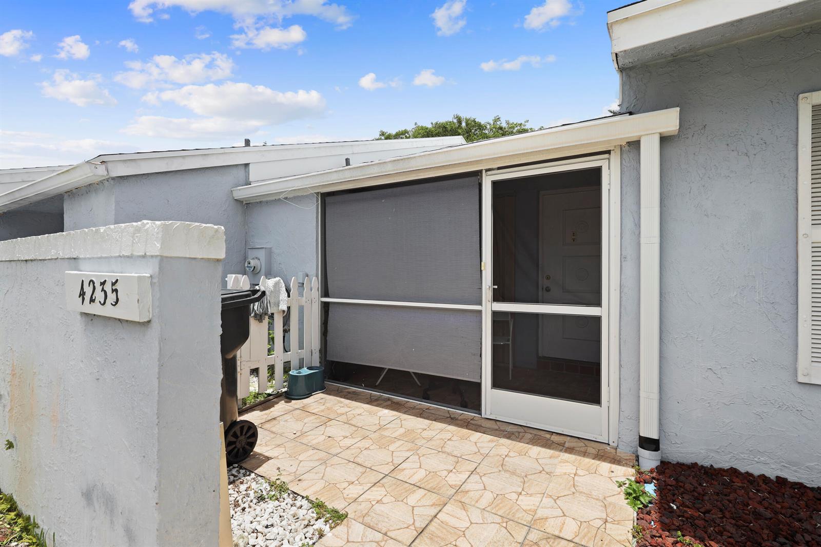 A tiled patio area features a screened enclosure with a door and a privacy shade — 4235 Lucerne Villas Lane, FL 33467, FL