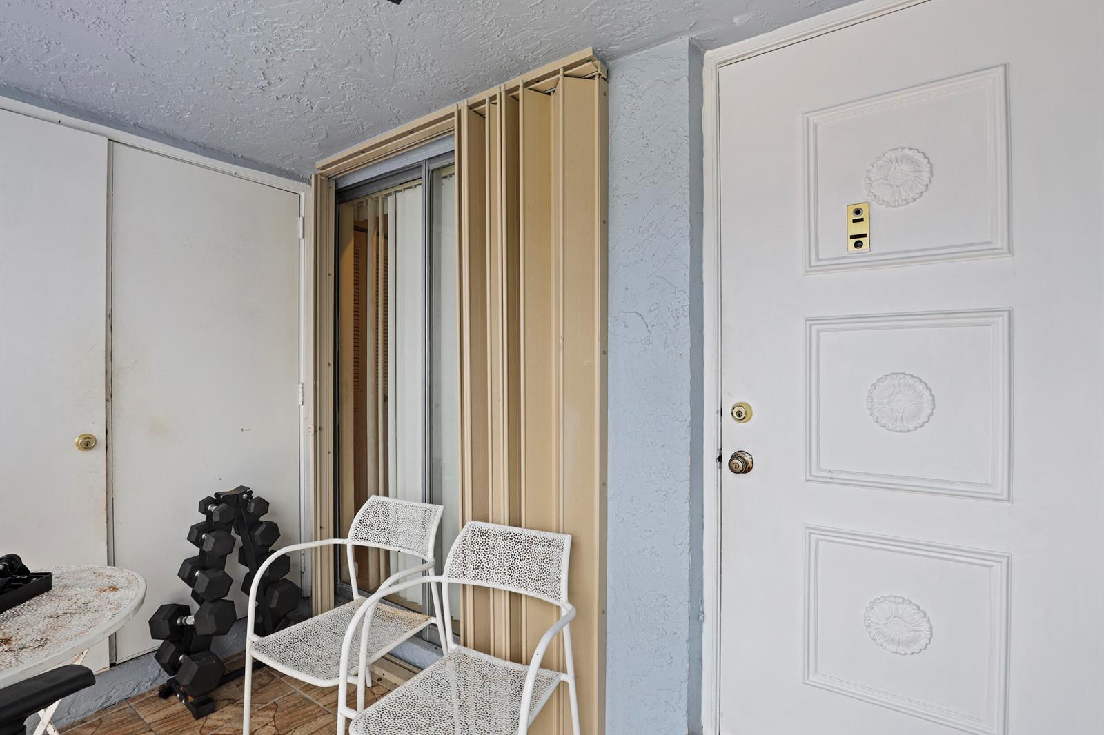 A white door and sliding glass door with beige shutters on a covered patio — 4235 Lucerne Villas Lane, FL 33467, FL