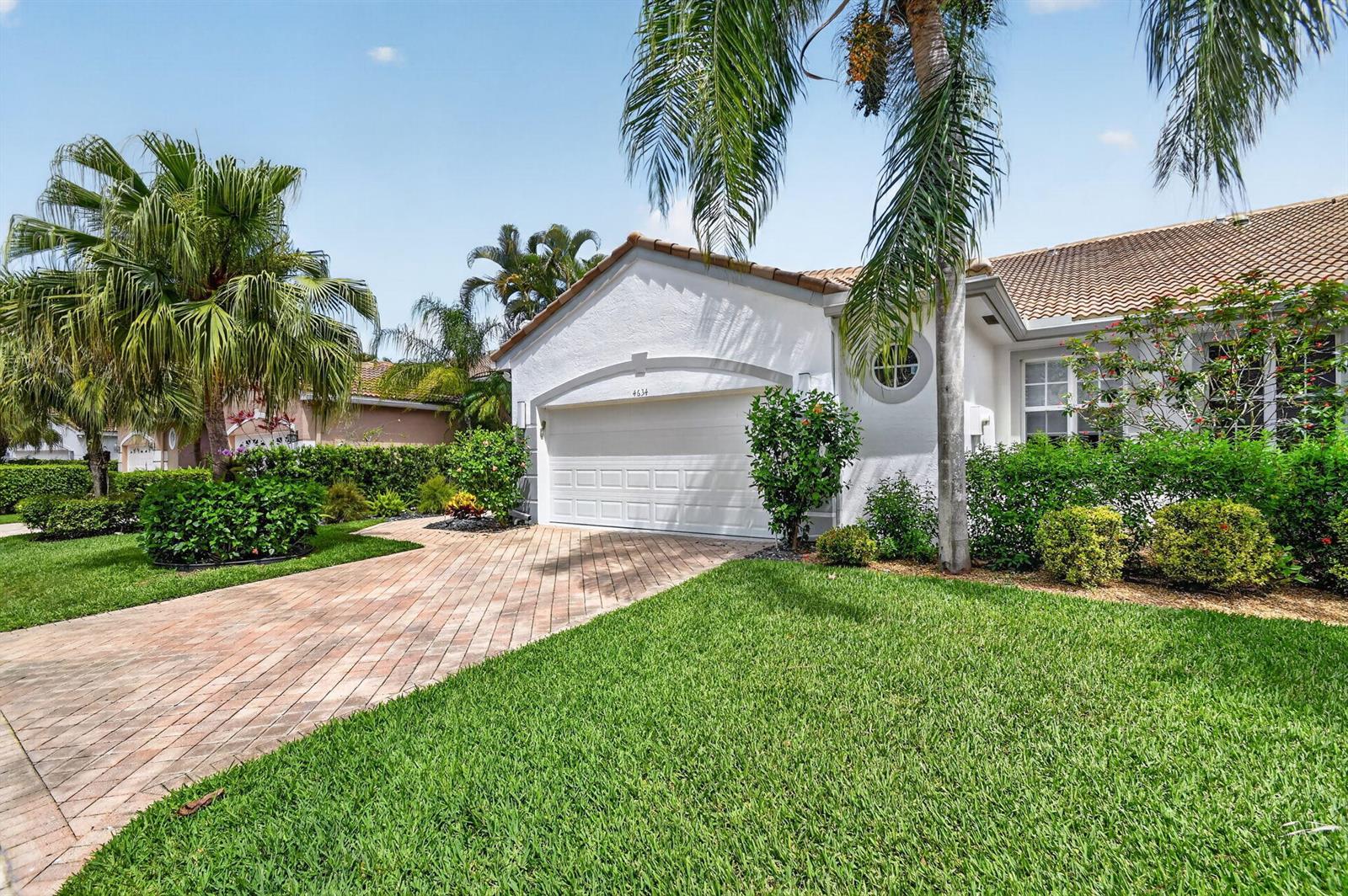 A white house with a brick paver driveway, a garage, and palm trees in the yard — 4634 Carlton Golf Drive, Lake Worth FL 33449, LAKE WORTH, FL