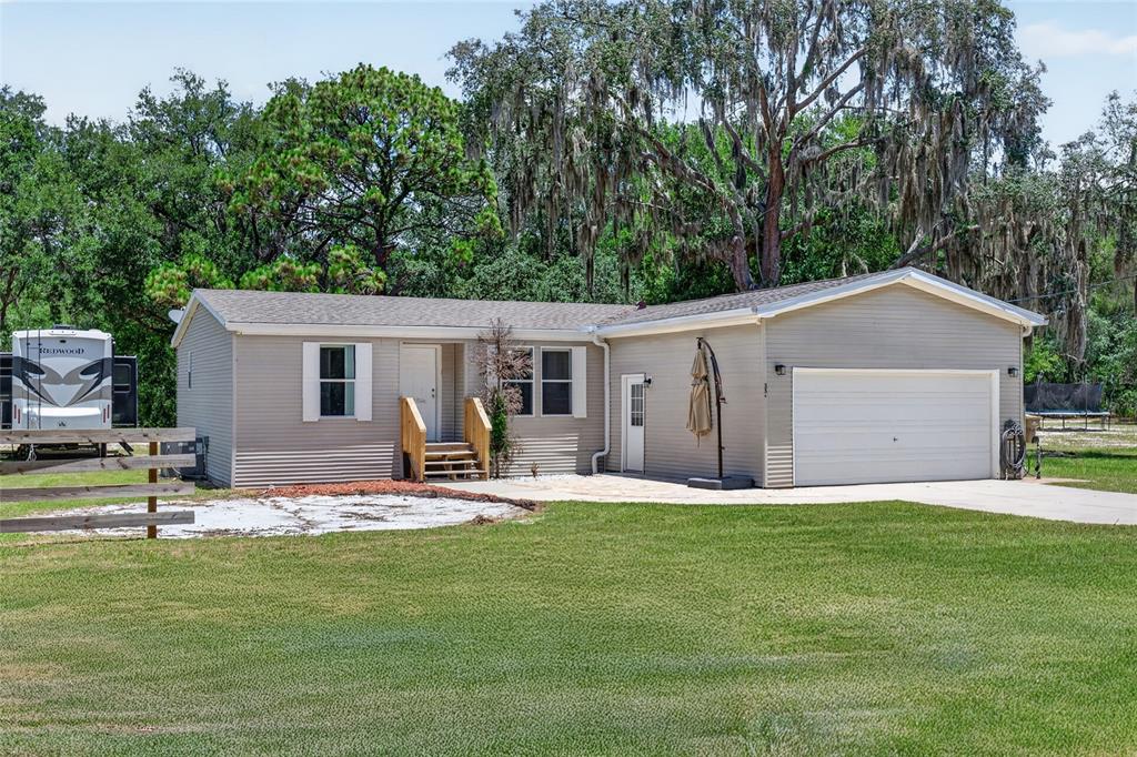 A single-story house with beige siding, a two-car garage, and a wooden front porch — 357 WALTER PLACE, FRUITLAND PARK, FL