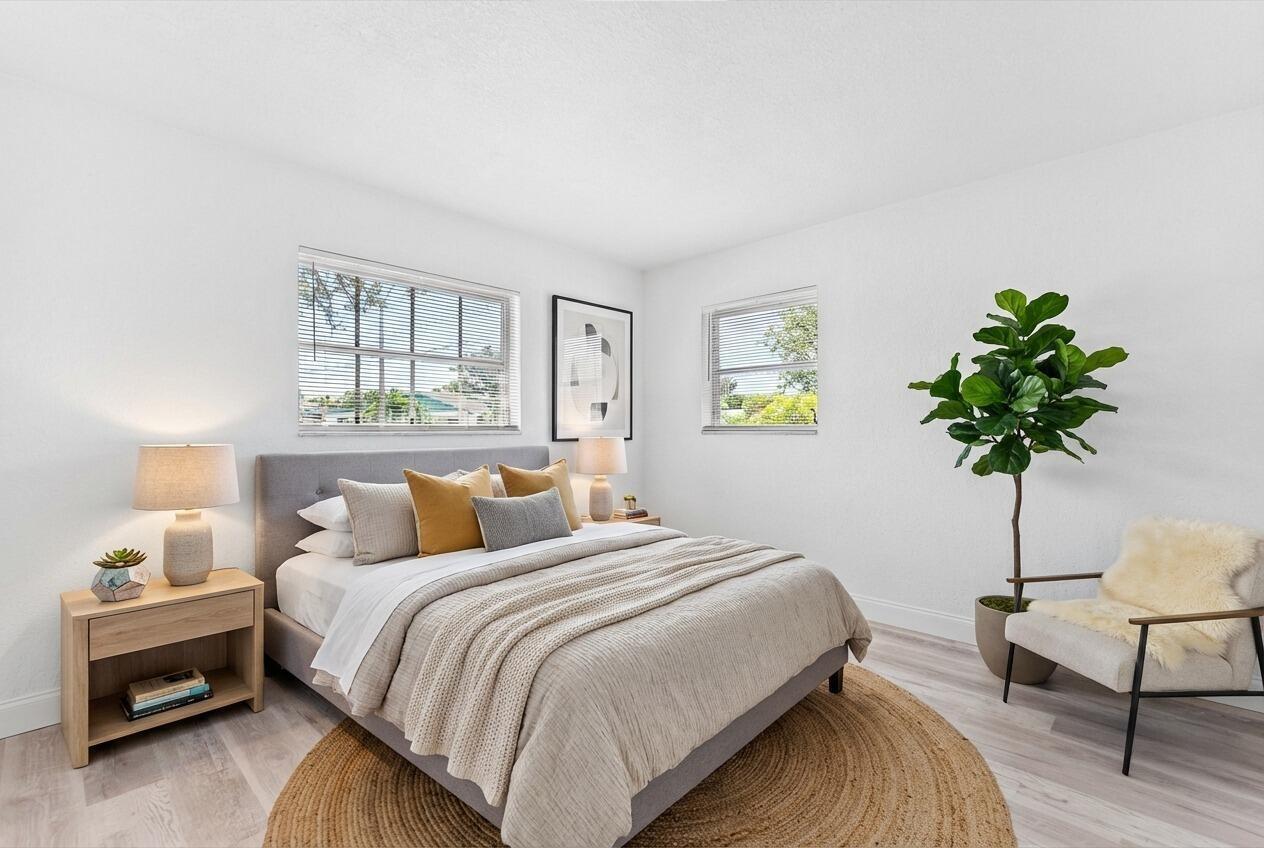 A bedroom with a gray bed, light wood nightstand, jute rug, and a potted plant — 308 Stillwater Drive, Jupiter FL 33458, JUPITER, FL