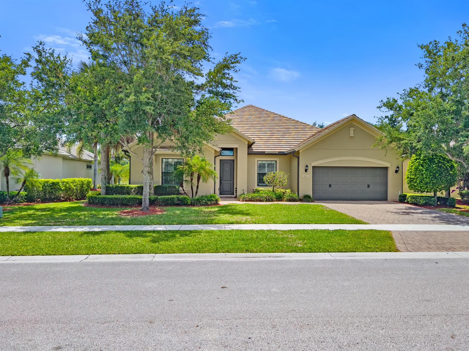 A single-story house with a tan exterior, a gray garage door, and a landscaped front yard — 4591 Siena Circle, Wellington FL 33414, WELLINGTON, FL