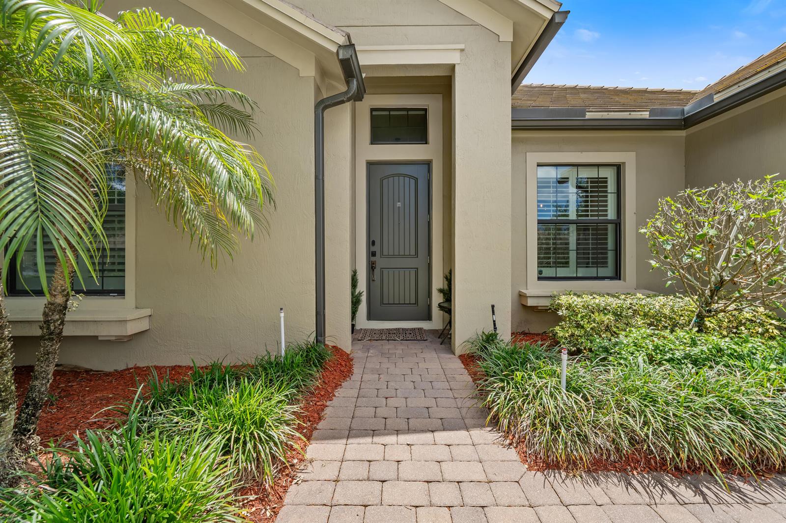 A paved walkway leads to the front entrance of a beige house with a dark door — 4591 Siena Circle, Wellington FL 33414, WELLINGTON, FL