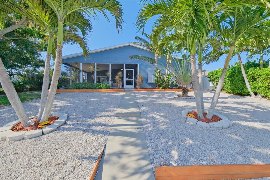 A blue house with a screened-in porch, gravel yard, and palm trees under a clear sky — 6811 GEORGIA AVENUE, BRADENTON, FL