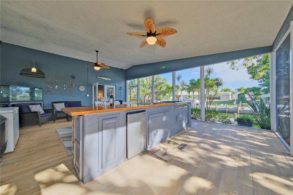 A covered outdoor kitchen and living area features a wooden bar, blue cabinetry, and screens — 6811 GEORGIA AVENUE, BRADENTON, FL