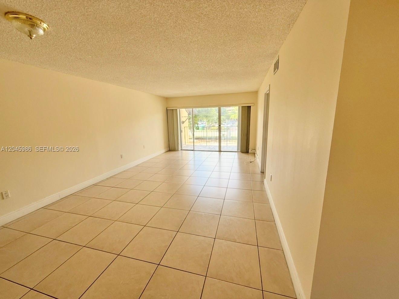 An empty room features beige tile flooring, light-colored walls, and a sliding glass door — 1975 W 44th Pl # 203, Hialeah FL 33012, HIALEAH, FL