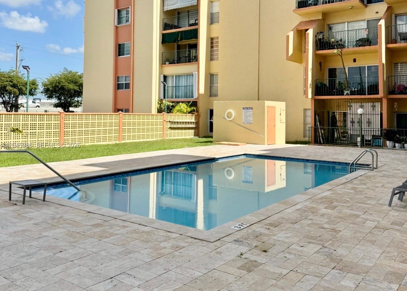 A rectangular swimming pool sits on a stone patio in front of a multi-story apartment building — 1975 W 44th Pl # 203, Hialeah FL 33012, HIALEAH, FL