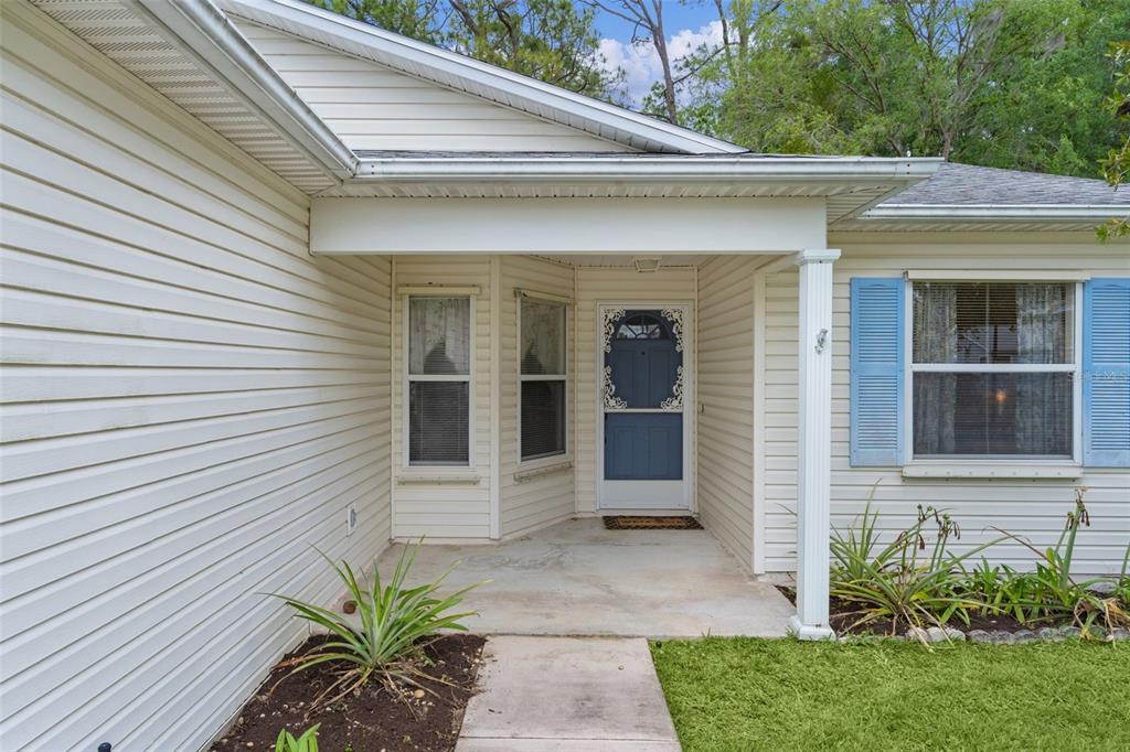 The exterior of a house features beige vinyl siding, a covered porch, and blue shutters — 413 WESTWOOD DRIVE, LEESBURG, FL