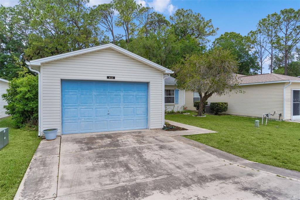 A single-story house with light siding, a blue garage door, and a concrete driveway — 413 WESTWOOD DRIVE, LEESBURG, FL