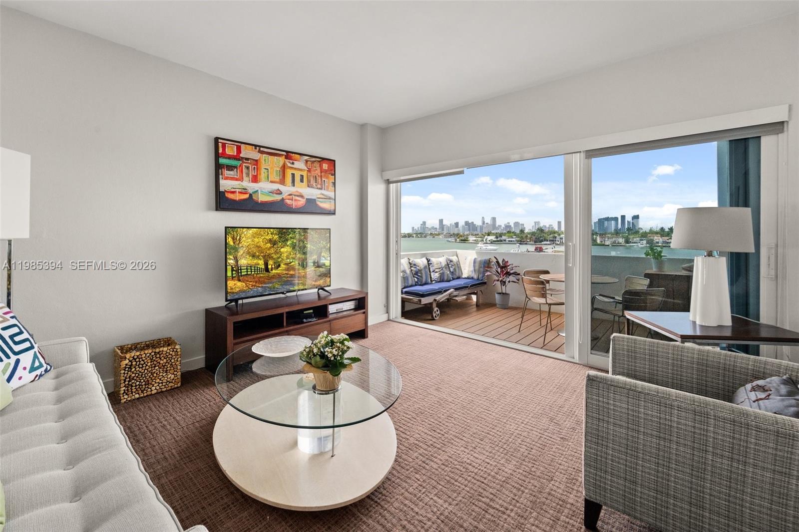 A living room features a glass coffee table, television, and a balcony overlooking a city — 3 Island Ave # 04I, Miami Beach FL 33139, MIAMI BEACH, FL