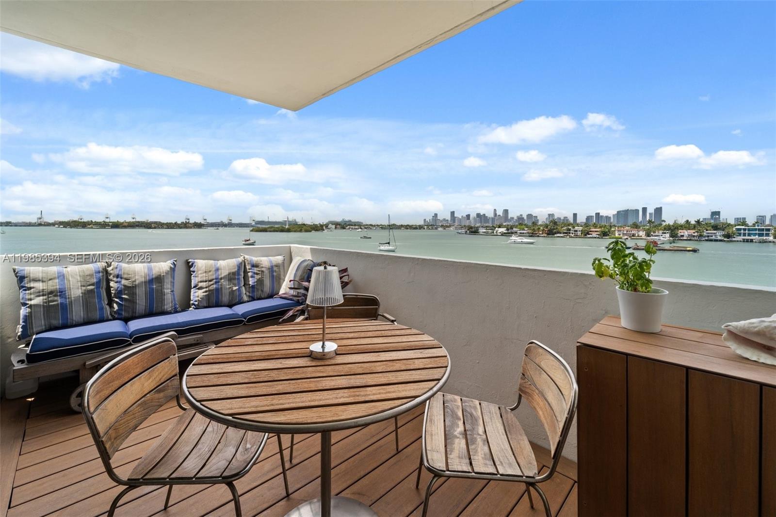 A balcony features a wooden table, chairs, a bench with pillows, and a waterfront view — 3 Island Ave # 04I, Miami Beach FL 33139, MIAMI BEACH, FL