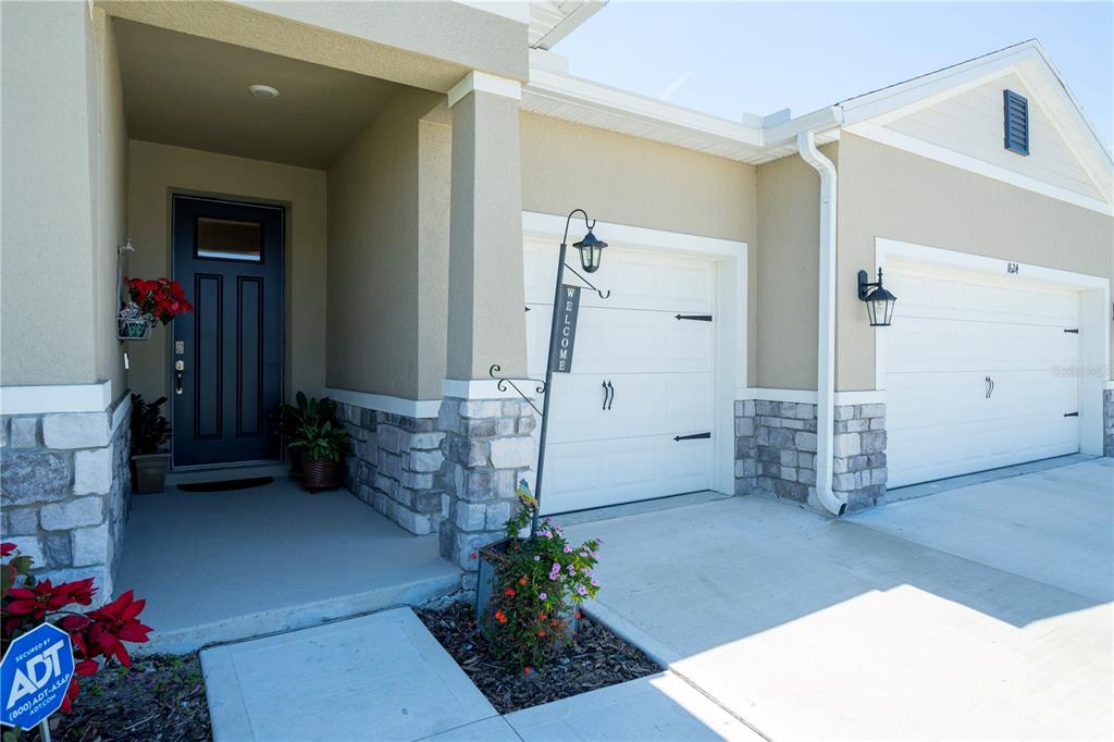 A beige house exterior features a dark front door, stone accents, and two garage doors — 1624 BARBERRY DRIVE, KISSIMMEE, FL