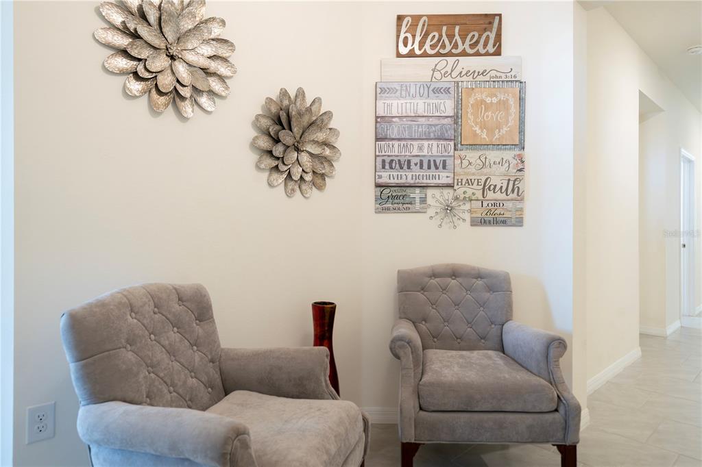 Two gray tufted armchairs sit in a corner with wall art and metal floral decorations — 1624 BARBERRY DRIVE, KISSIMMEE, FL