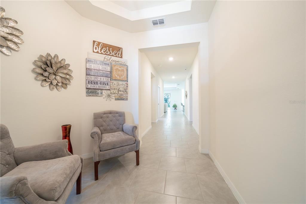 A hallway with light tile flooring features two grey armchairs and wall-mounted decorative art — 1624 BARBERRY DRIVE, KISSIMMEE, FL