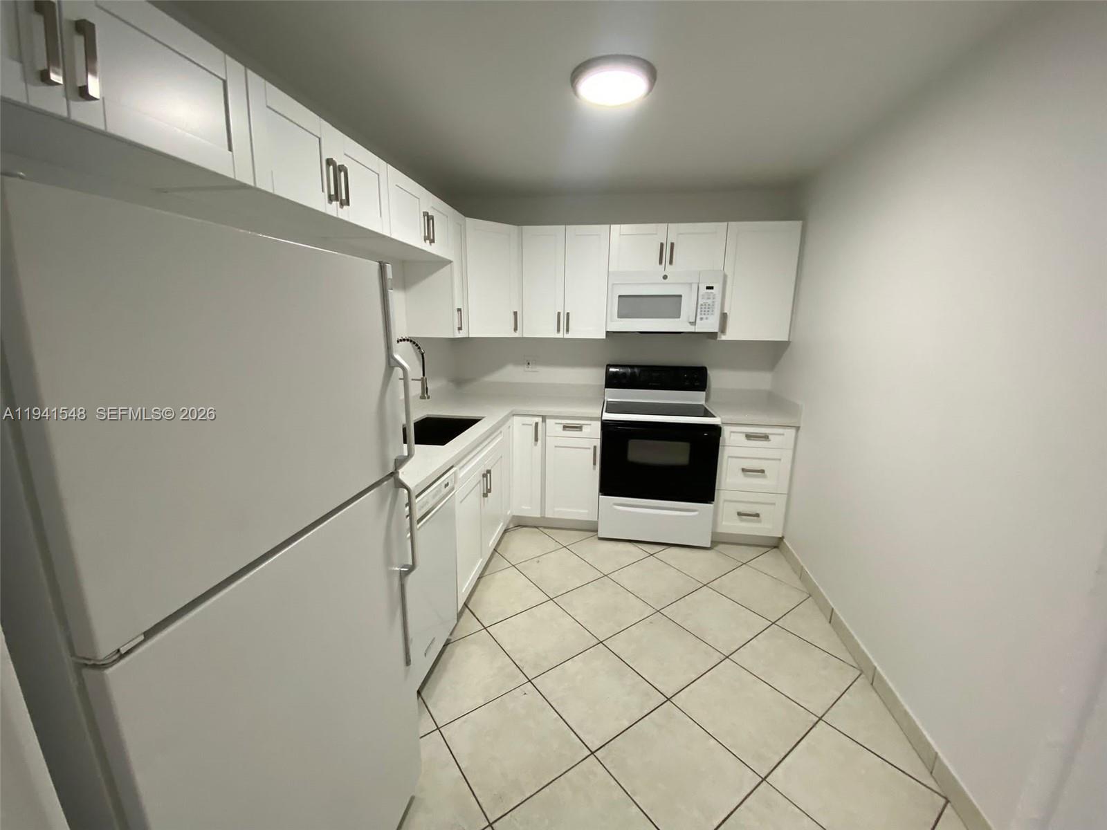 A galley kitchen features white cabinets, white appliances, and light-colored tile flooring — 4344 NW 9th Ave # 3D, Deerfield Beach FL 33064, DEERFIELD BEACH, FL