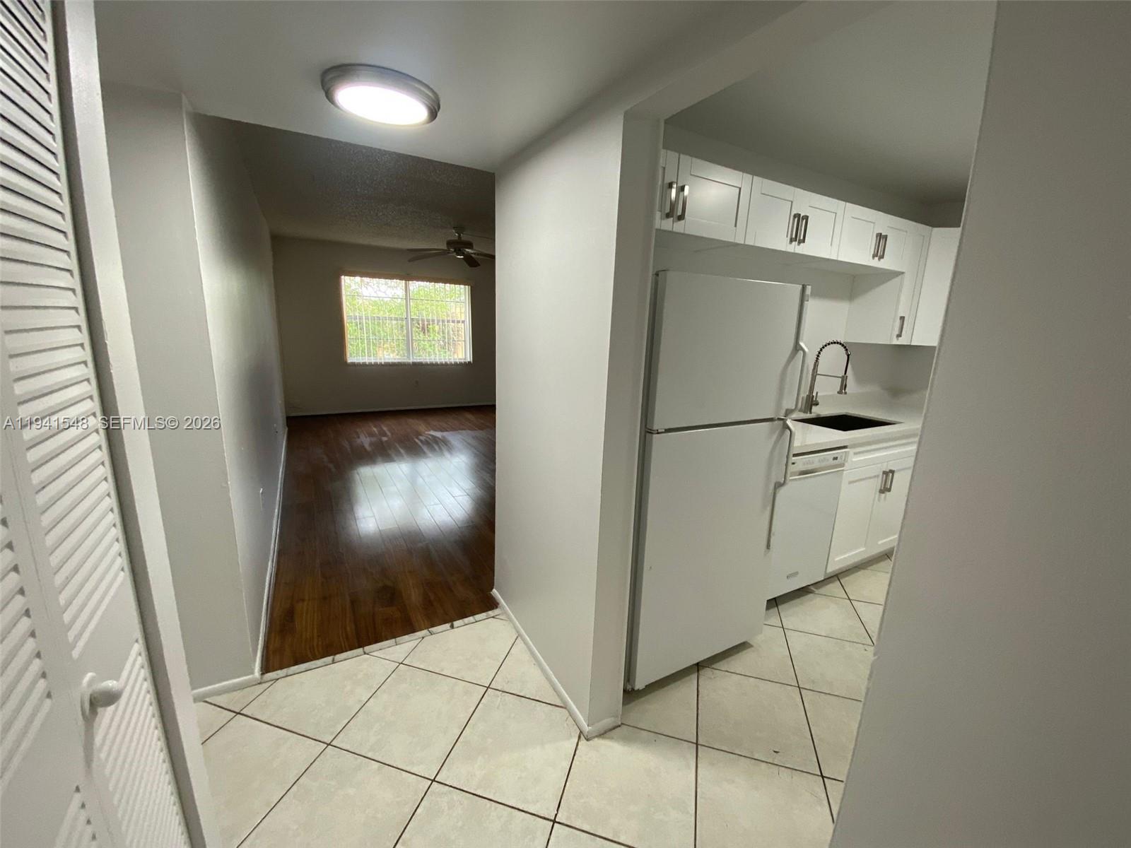 A kitchen with white cabinets and appliances opens into a living area with wood floors — 4344 NW 9th Ave # 3D, Deerfield Beach FL 33064, DEERFIELD BEACH, FL