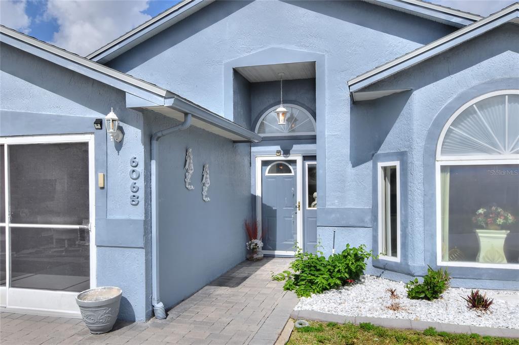 The exterior of a light blue house features a paved walkway leading to the front door — 6068 SWALLOW DRIVE, LAKELAND, FL