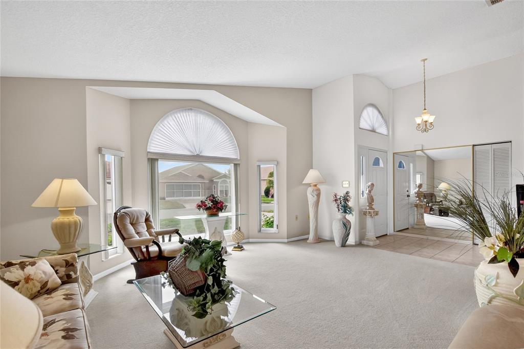 A bright living room features carpeted floors, a large arched window, and a mirrored wall — 6068 SWALLOW DRIVE, LAKELAND, FL