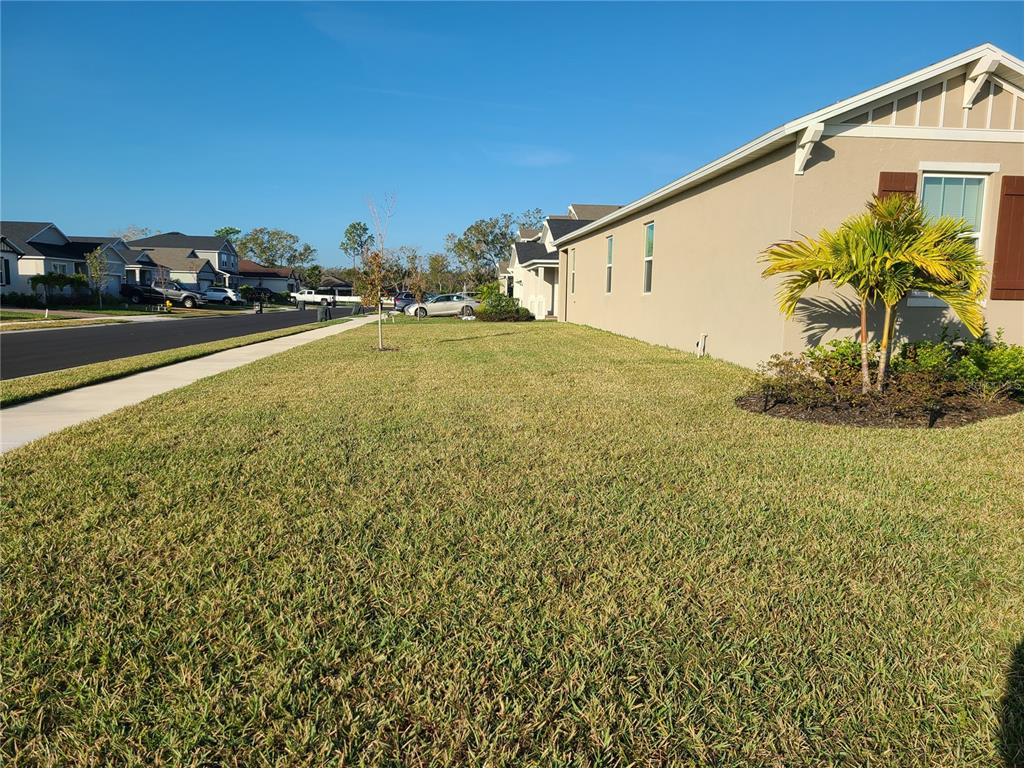 A side view of a suburban house with a large lawn and a paved street — 5736 143RD COURT E, BRADENTON, FL