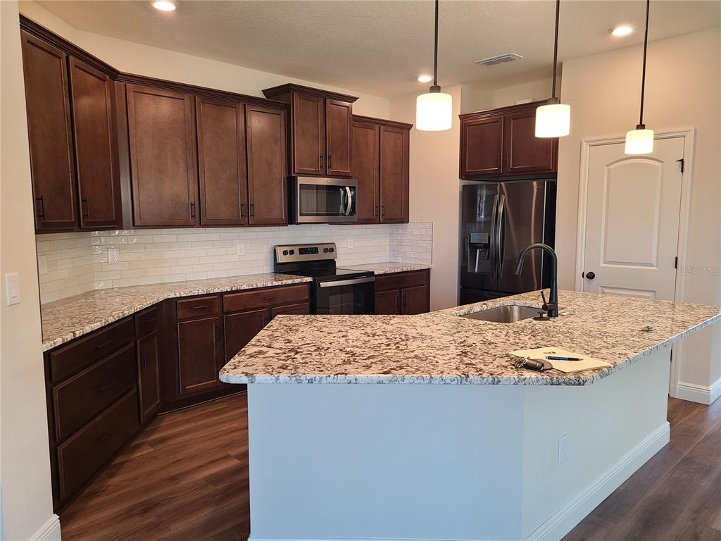 A kitchen features dark wood cabinets, granite countertops, a center island, and stainless steel appliances — 5736 143RD COURT E, BRADENTON, FL
