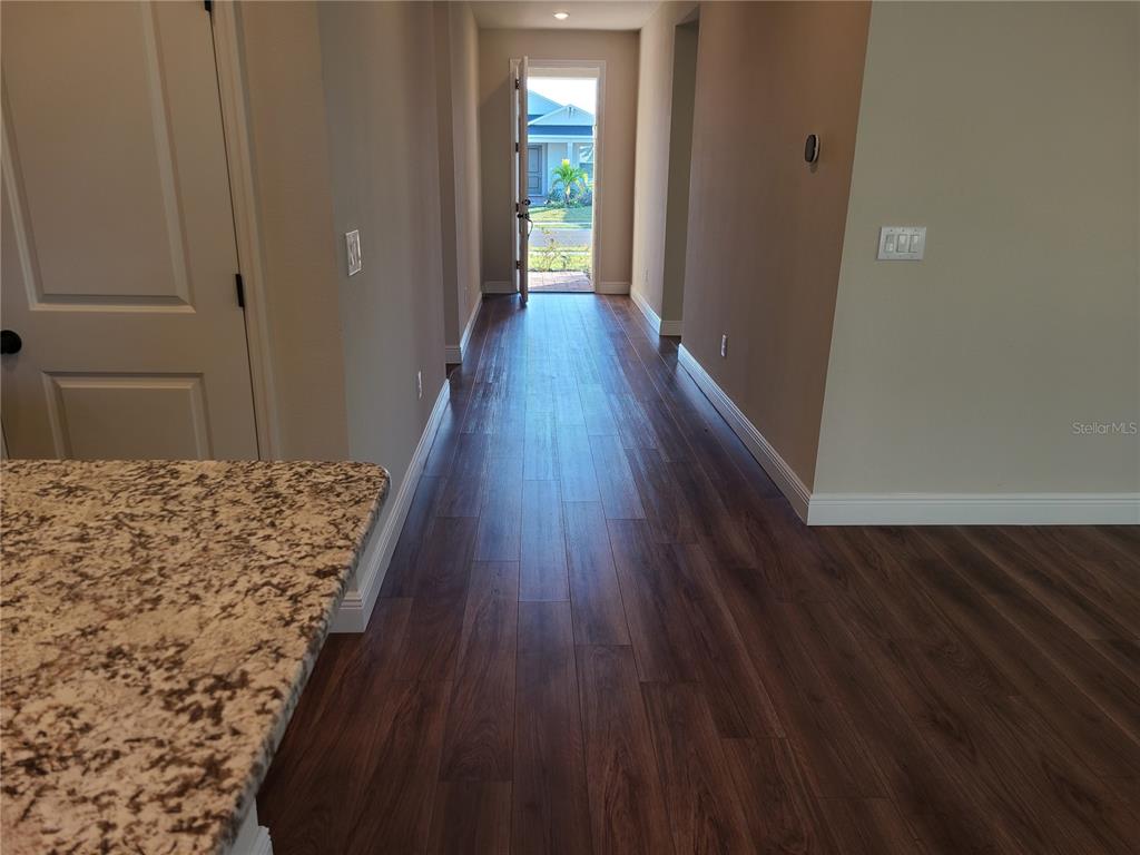 A hallway with dark wood-look flooring leads to an open front door — 5736 143RD COURT E, BRADENTON, FL