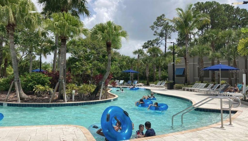 A resort-style swimming pool with a lazy river, palm trees, and lounge chairs — 14501 GROVE RESORT AVENUE UNIT 2129, WINTER GARDEN, FL