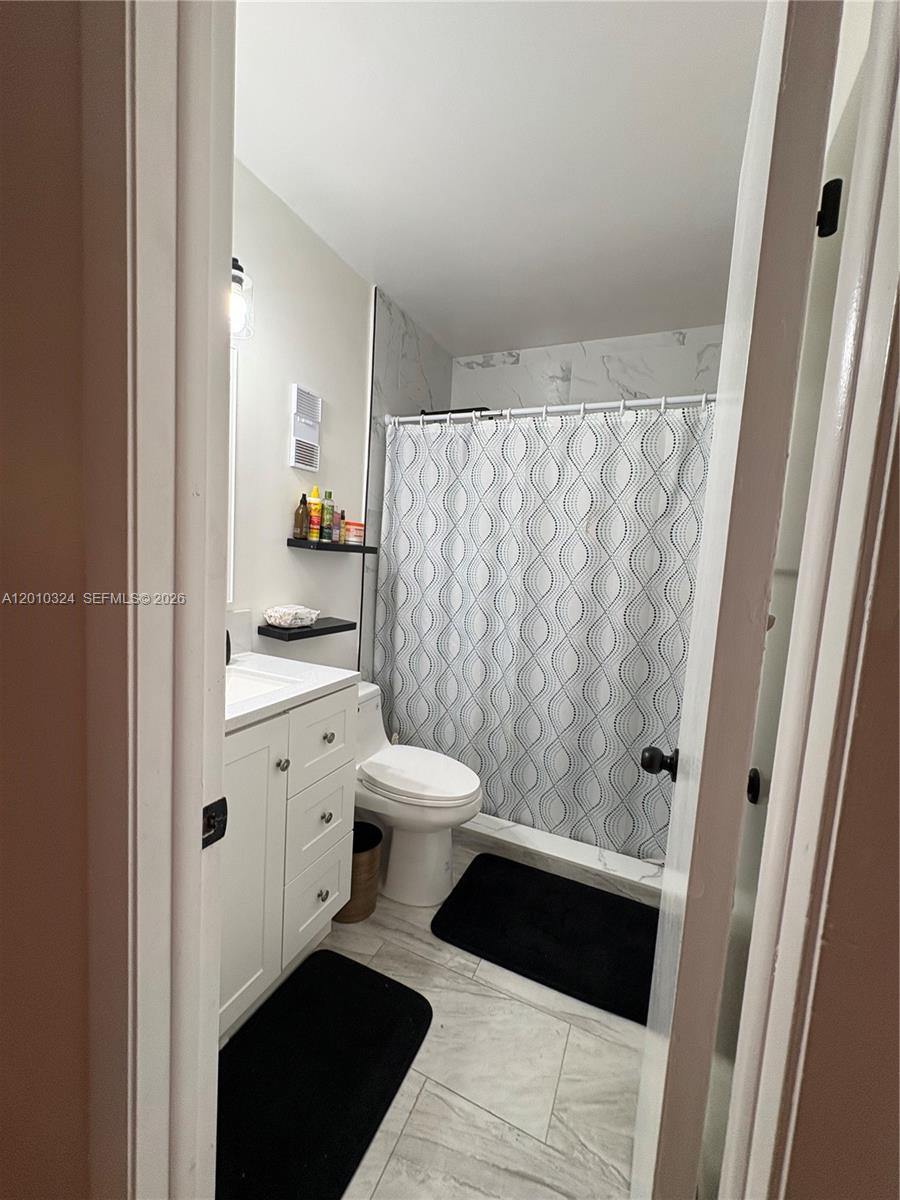 A small bathroom features a white vanity, a toilet, and a shower with patterned curtains — 5424 Gate Lake Rd # 5424, Tamarac FL 33319, TAMARAC, FL