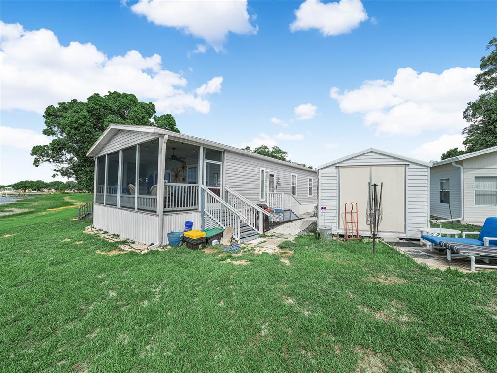 A manufactured home with a screened-in porch stands next to a shed on a lawn — 29 WOODRUFF WAY, LAKE WALES, FL