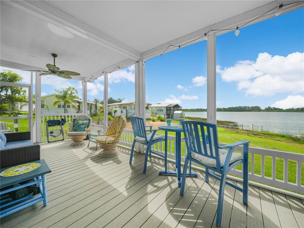 A screened-in porch with outdoor furniture overlooks a lake and neighboring homes — 29 WOODRUFF WAY, LAKE WALES, FL