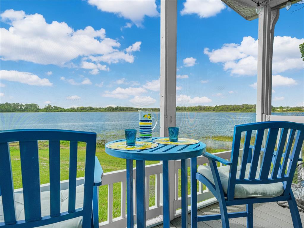 A blue bistro set sits on a screened-in porch overlooking a lake and grassy yard — 29 WOODRUFF WAY, LAKE WALES, FL