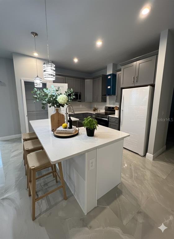 A modern kitchen features a white island with bar stools, gray cabinets, and marble-look flooring — 373 AMBERJACK, POINCIANA, FL