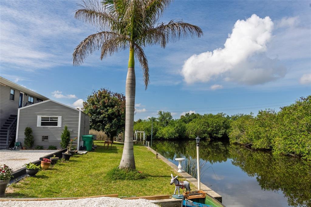 A palm tree stands on a grassy lawn beside a small house and a canal — 29103 ORVA DRIVE, PUNTA GORDA, FL