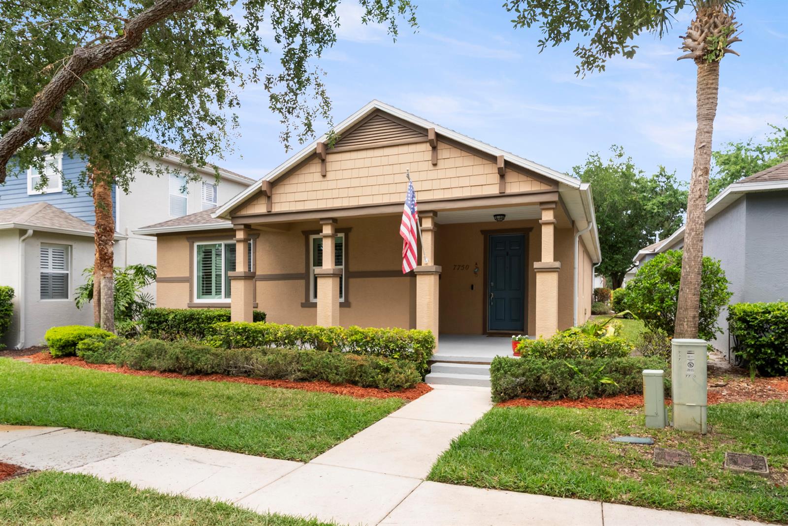 A tan, single-story house with a front porch, American flag, and manicured landscaping — 7750 15th Street, Vero Beach FL 32966, VERO BEACH, FL