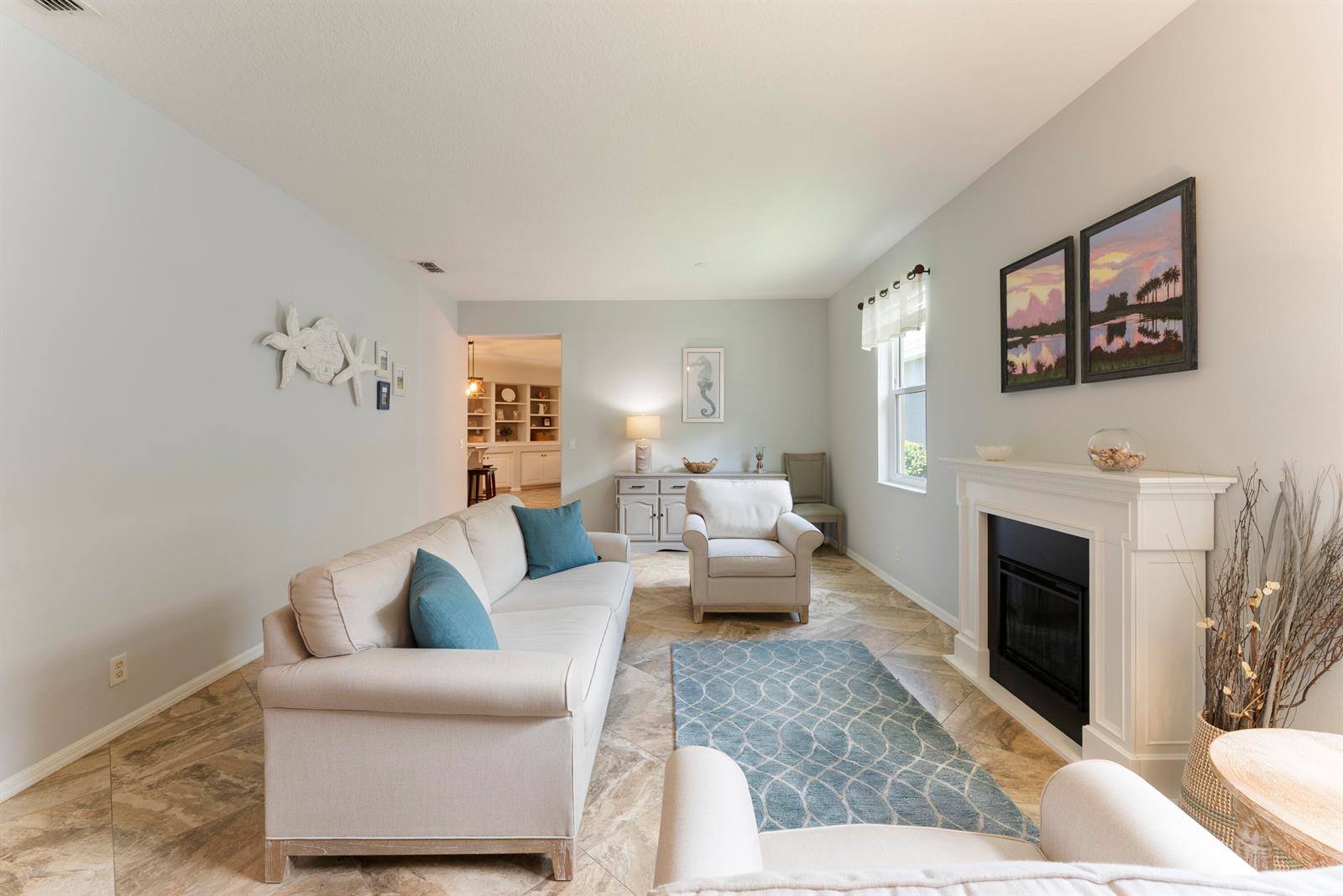 A living room features a fireplace, light-colored furniture, tile flooring, and coastal-themed wall decor — 7750 15th Street, Vero Beach FL 32966, VERO BEACH, FL
