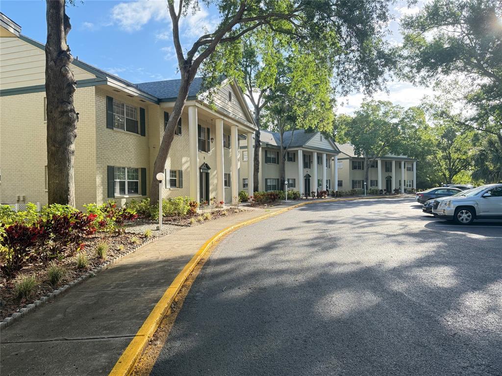 An exterior view of a multi-story apartment complex with white columns and a parking lot — 117 N MERCURY AVENUE UNIT 117, CLEARWATER, FL