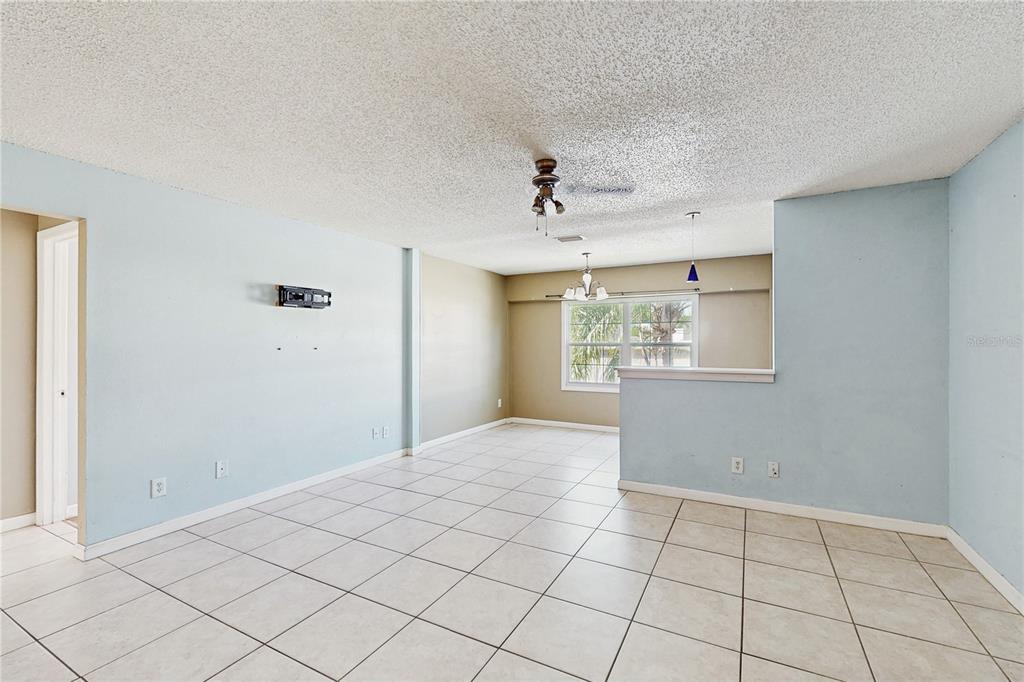 An open-concept living and dining area features light blue walls, beige tile flooring, and popcorn ceilings — 117 N MERCURY AVENUE UNIT 117, CLEARWATER, FL